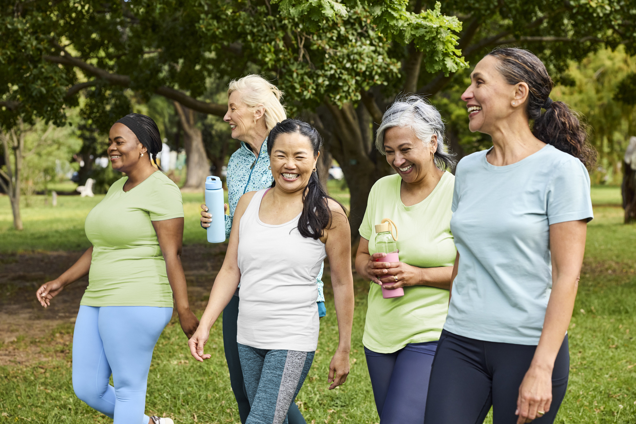 Happy group of women talking with each other in park. Multiracial female friends are walking together after yoga routine. They are wearing sports clothing.